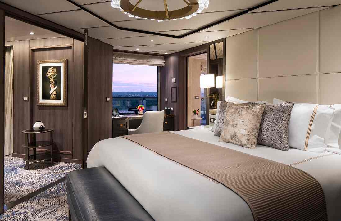 Pinnacle Suite stateroom with king bed, separate sitting area, artwork, and large window with ocean view.