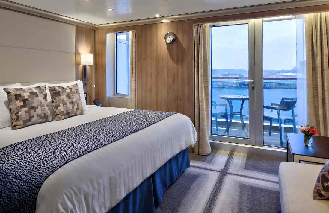 Signature Suite stateroom with king bed and sliding glass doors to a private balcony with ocean view.