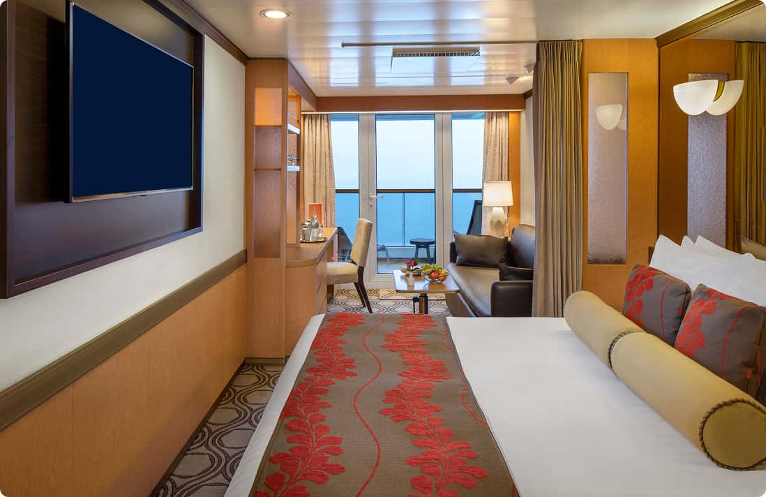 Vista Suite stateroom with king bed, seating area, and private balcony overlooking ocean on Holland America cruise ship.