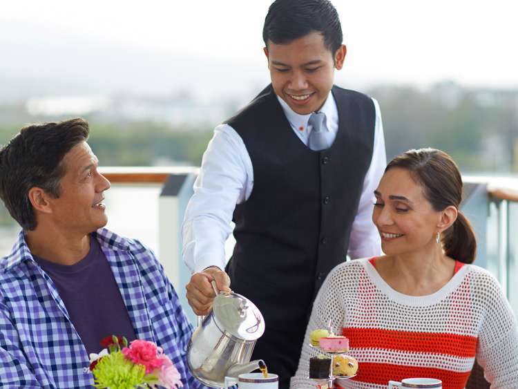 Picture of a waiter pouring tea for a couple enjoying a variety of deserts on a world cruise