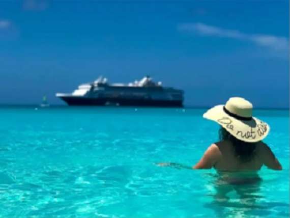 Woman swimming in crystal blue Caribbean water with a Holland America Line cruise ship sailing in the background.
