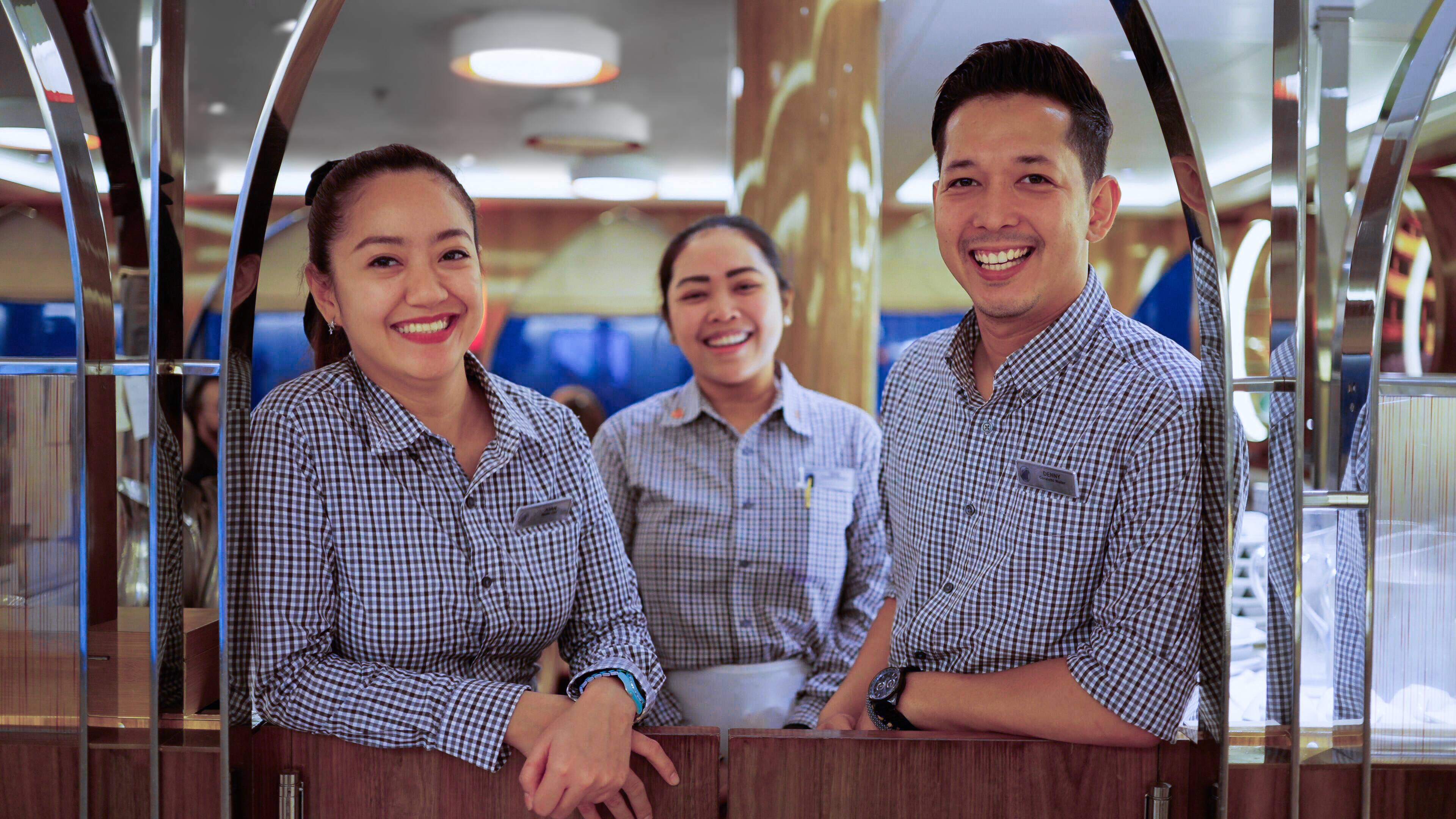 3 Holland America Line on-board employees smiling.