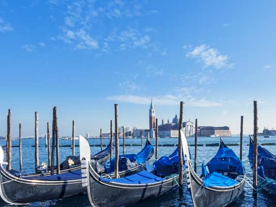 row of gondolas in Venice canal with cathedral in the background