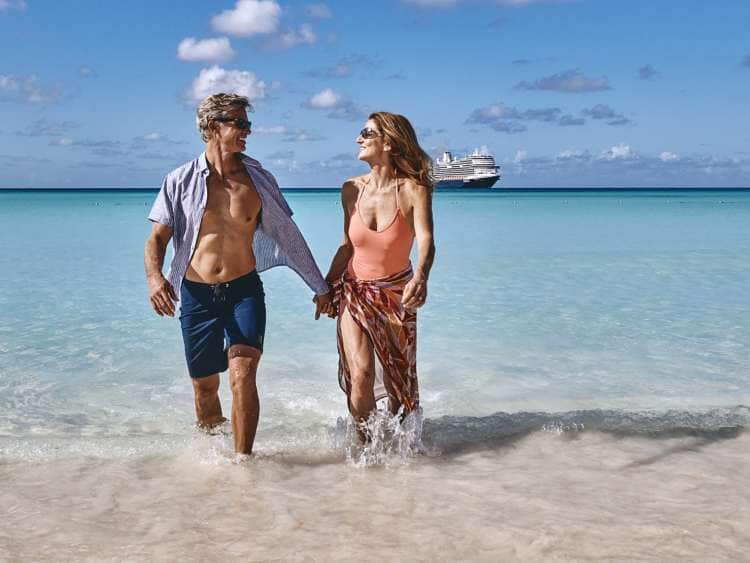 Couple walking out of turquoise sea water and a cruise ship on the horizon