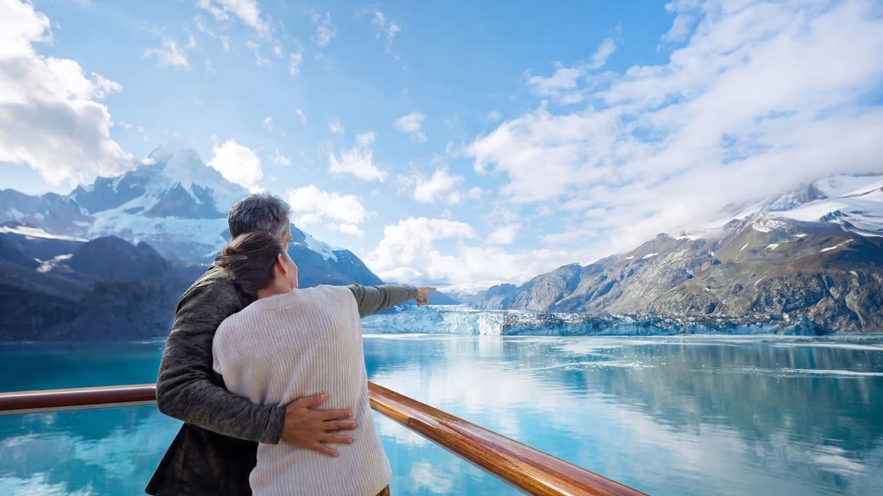 Guests viewing a glacier and mountain landscape from the deck of a cruise ship in Alaska.