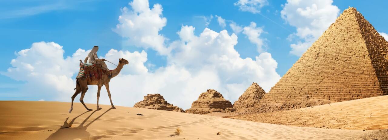 A man on a camel heading towards the pyramids in Egypt.