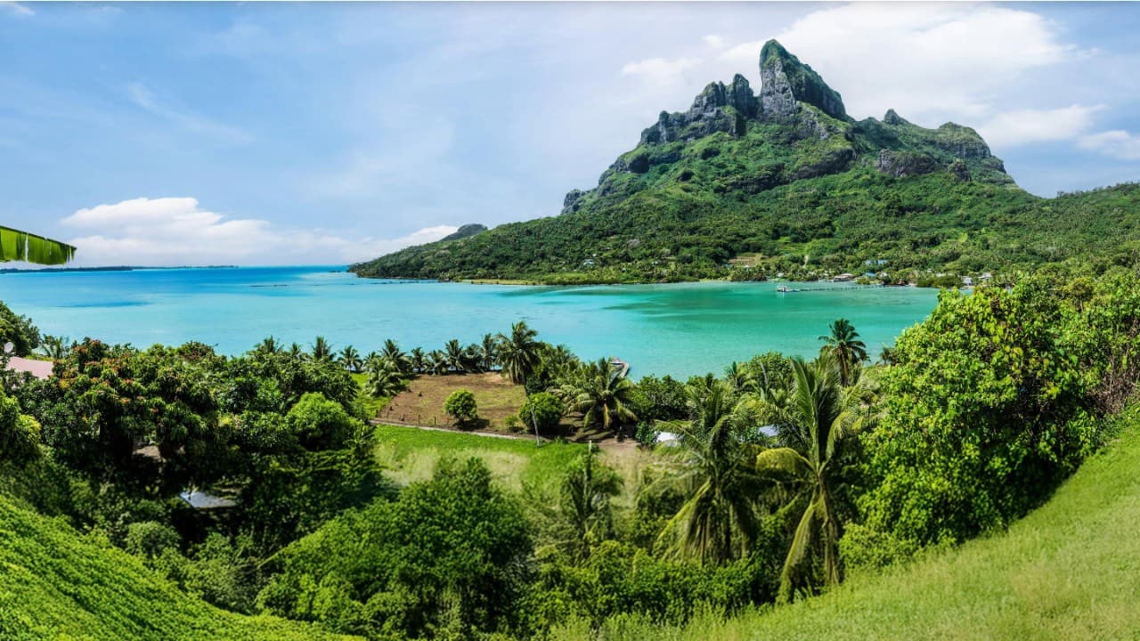 Bora Bora lagoon with turquoise water and lush green Mount Otemanu under clear blue sky.
