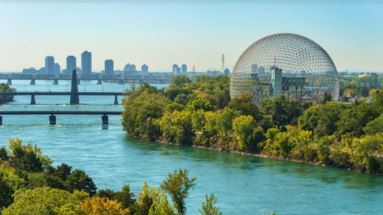 View of Montreal’s Biosphere overlooking the Saint Lawrence River, with bridges, tree-lined islands, and the city skyline in the background.