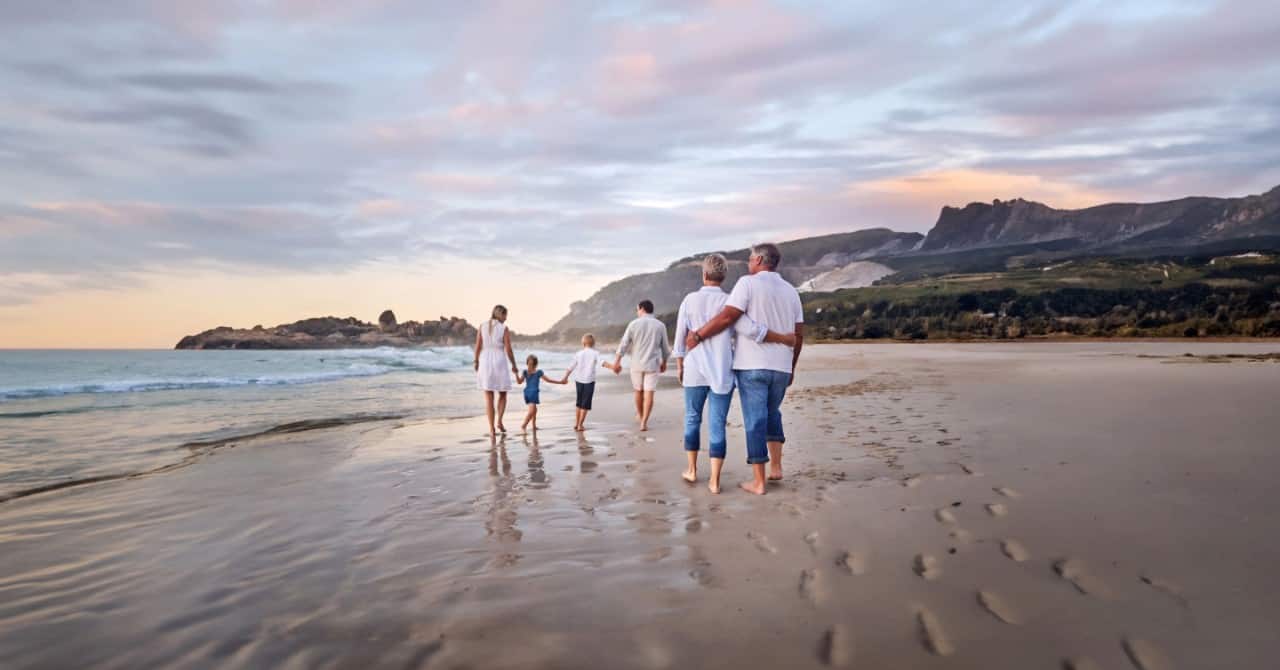 Multigenerational family walks along a beach at a coastal destination during a Holland America cruise.