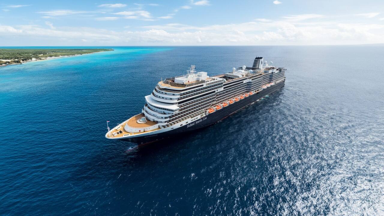 Nieuw Statendam cruise ship sailing on clear blue ocean near a tropical coastline under a bright sky.