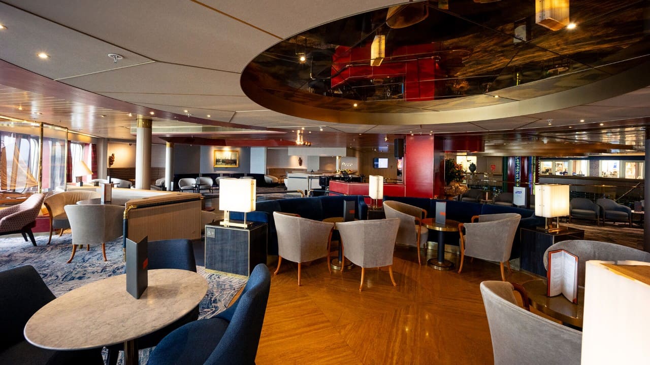 Spacious cruise ship lounge with modern seating, tables, and ambient lighting in an elegant indoor gathering space.