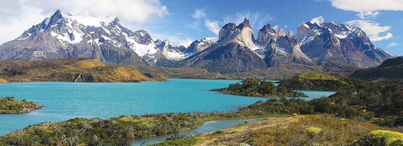 A body of water in the foreground with snow-capped mountains in the background.
