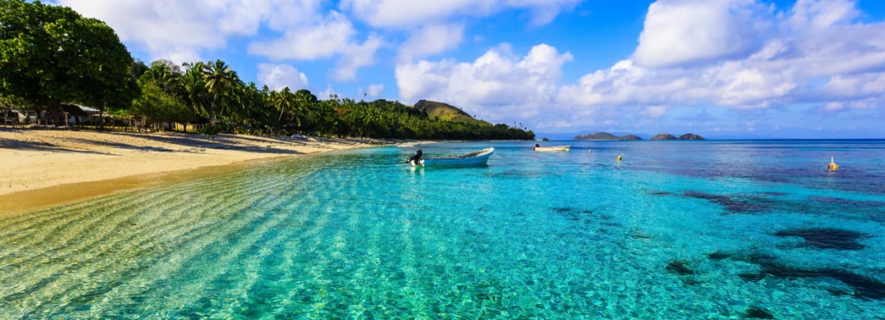 A view of the beach and a boat sitting in beautiful clear water in Fiji.