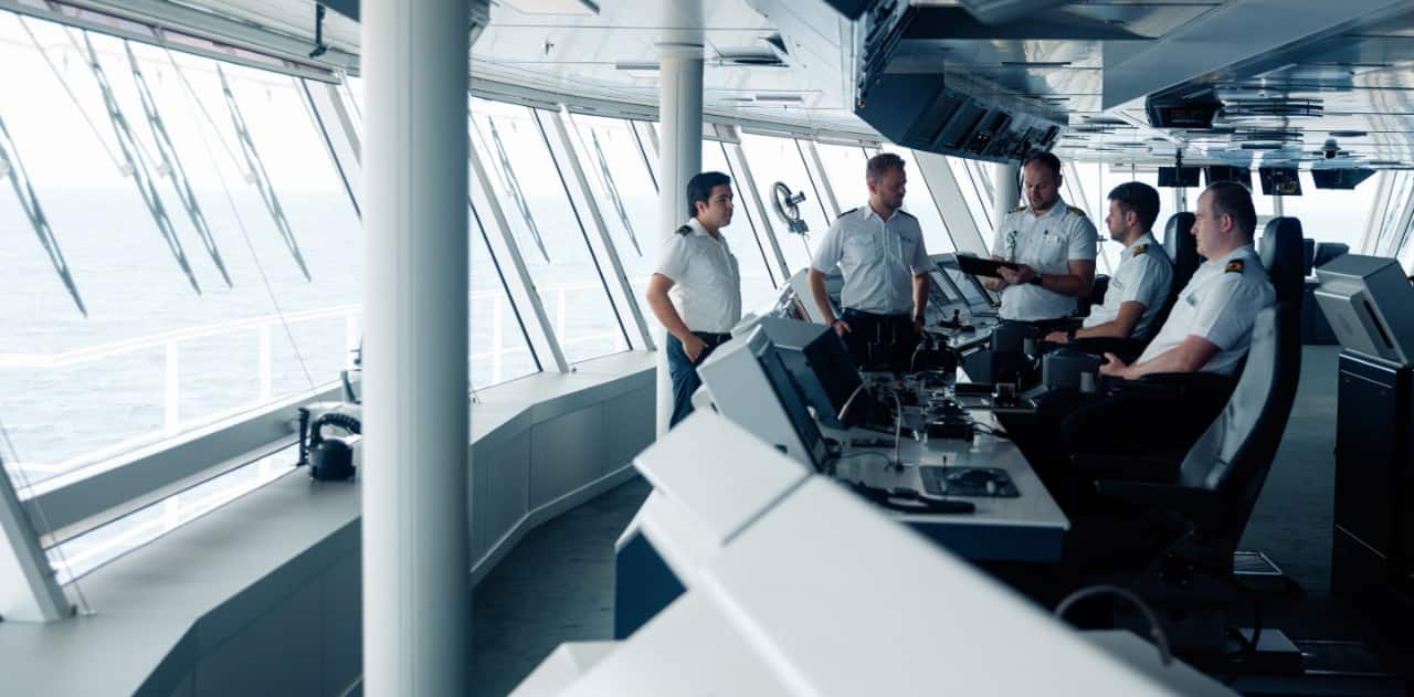Ship officers discussing navigation plans on a modern vessel bridge with ocean view.