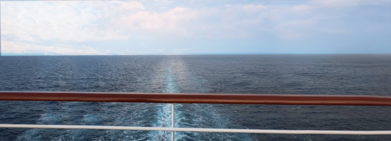 A view of the water from the deck on the back of a ship.