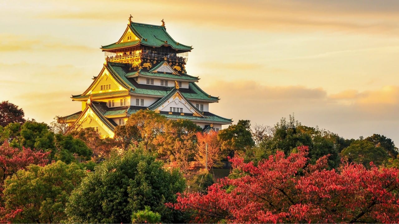 Osaka Castle at sunset surrounded by vibrant autumn foliage in Japan.