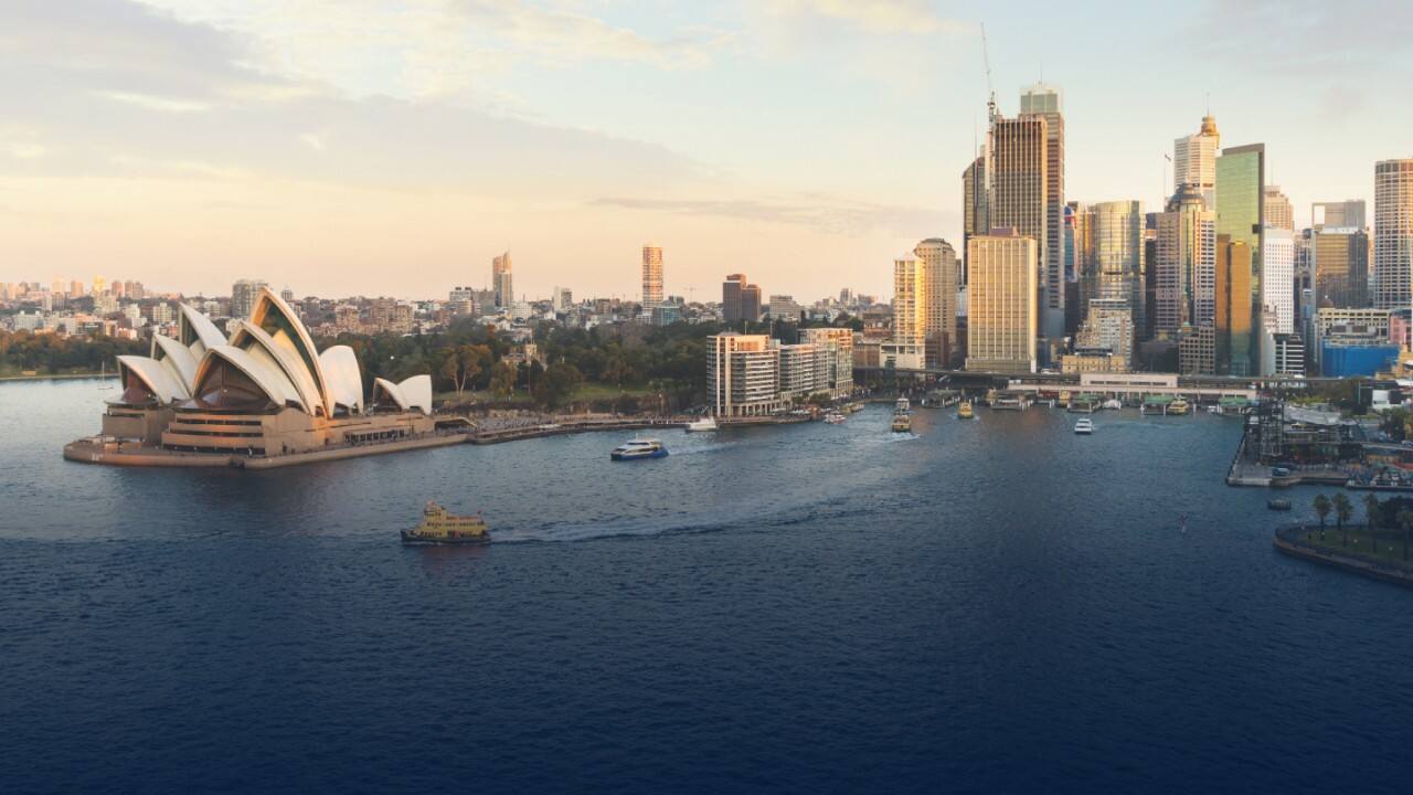 Sydney Harbour, Australia at sunset, featuring the iconic Sydney Opera House, city skyline, and boats on the water. 