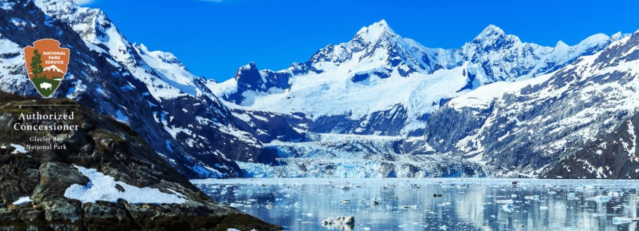 View of Glacier Bay across the inlet.  Logo of the national Park Service identifies Holland America Line as an authorized concessioner