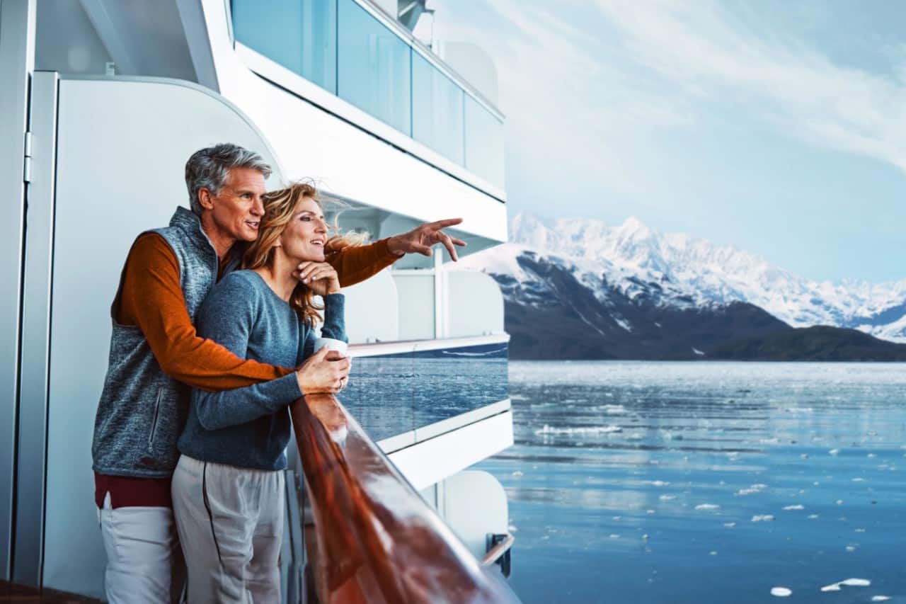 Couple on a cruise ship deck admiring Alaska’s snowy mountains and icy waters.