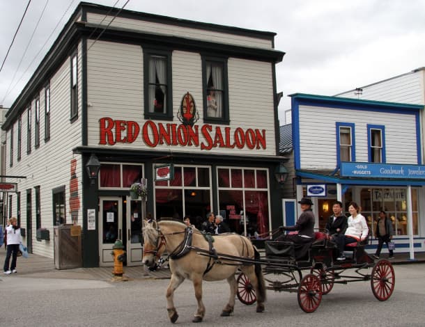 A horse-drawn carriage passes a historic building with "RED ONION SALOON" prominently displayed in downtown Skagway, Alaska