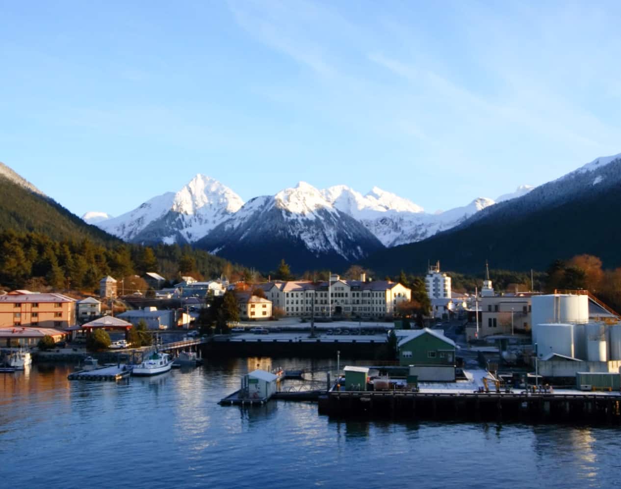 A scenic view of Sitka, Alaska, framed by snow-capped mountains and evergreen forests under a clear sky.