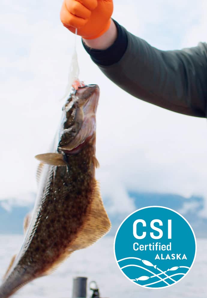 A person holds a freshly-caught fish in a net, with a "CSI Certified Alaska" logo present