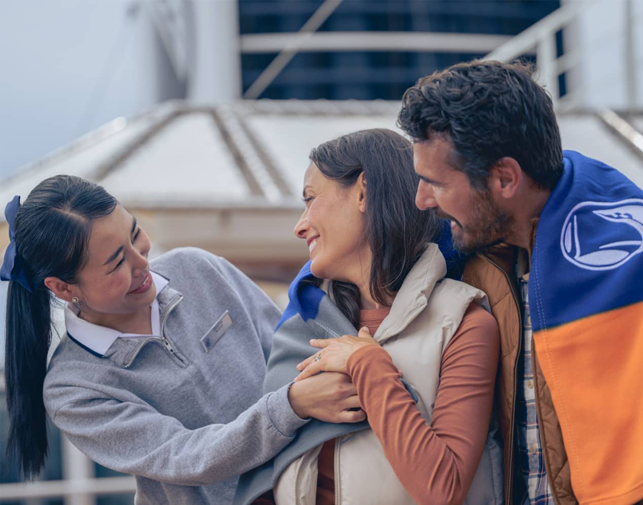 A smiling crew member brings a blanket to thankful guests on the deck of a Holland America cruise to Alaska