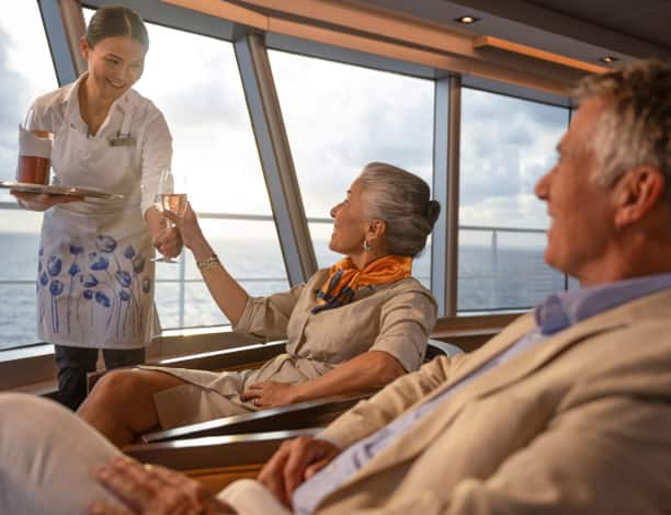A Holland America crew member brings drinks to a couple enjoying the Alaskan view