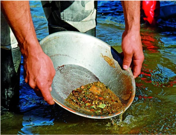 A man bends forward to pan for gold in river in the Yukon