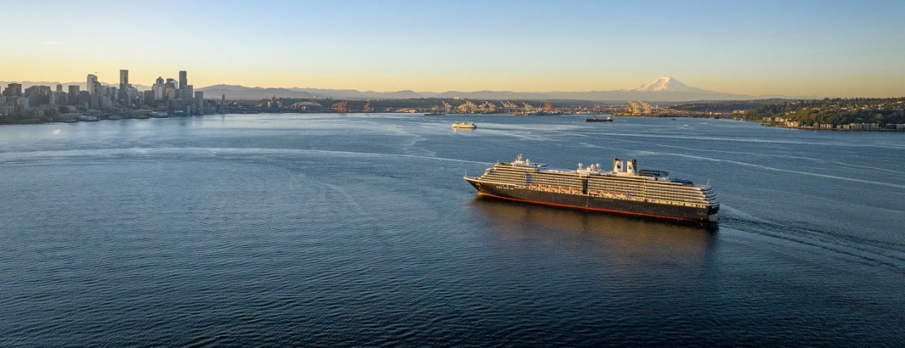 A kayak on turquoise water in Kenai Fjords National Park, Alaska, surrounded by forested mountains under a cloudy sky.