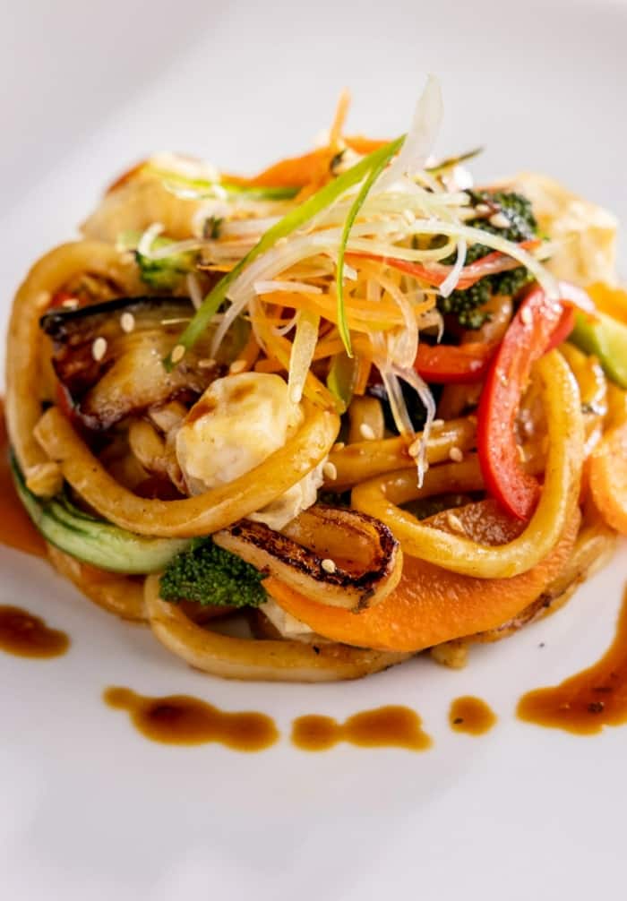 Udon noodles with fried tofu on a white plate