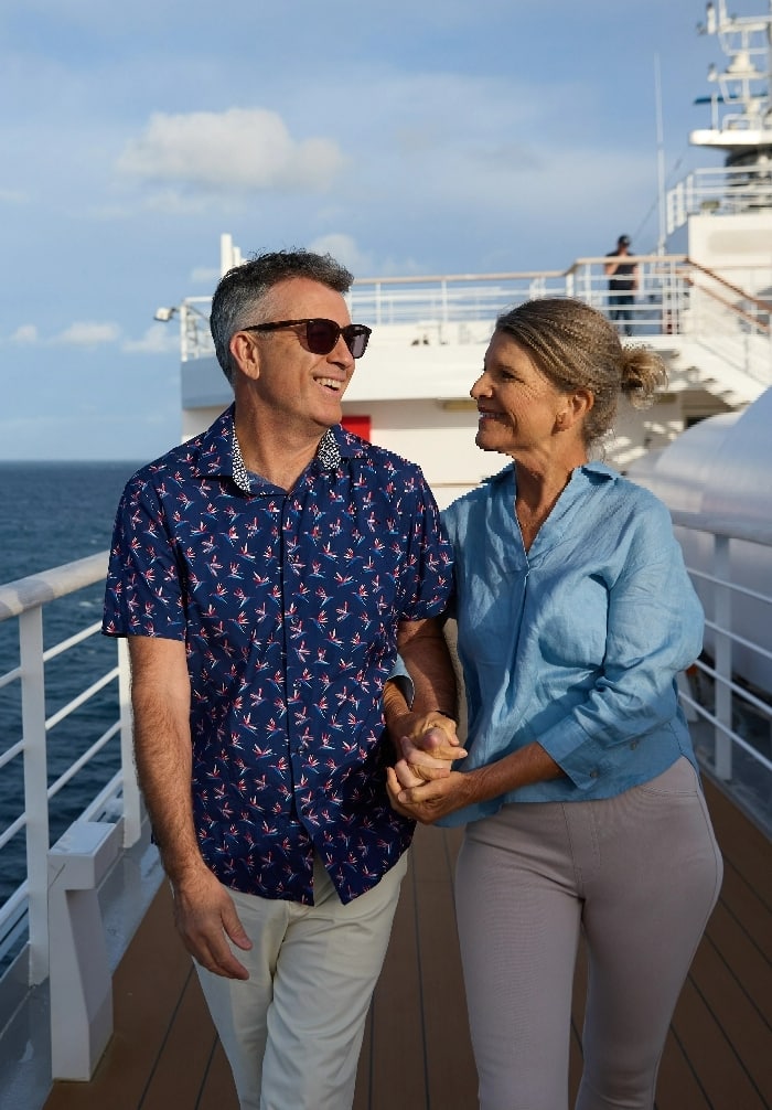 A couple walking hand in hand on the deck of a ship.