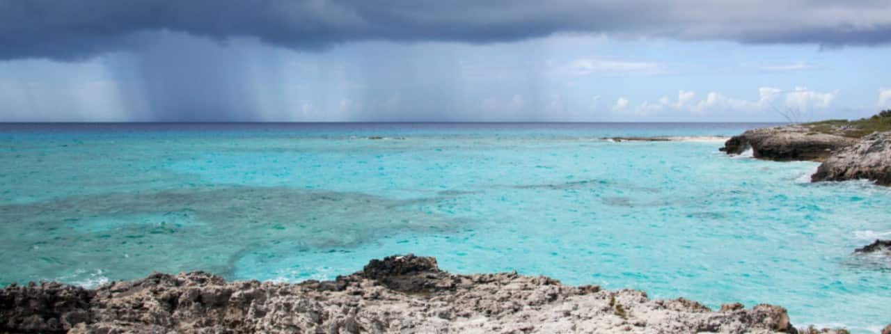 Dark storm clouds over turquoise waters and a rocky shoreline in the Bahamas. 