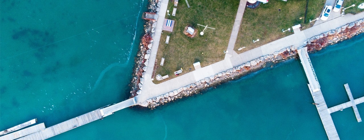Aerial view of a rocky peninsula in Suez, Egypt with a dock, benches, and picnic tables along a concrete path by the water.