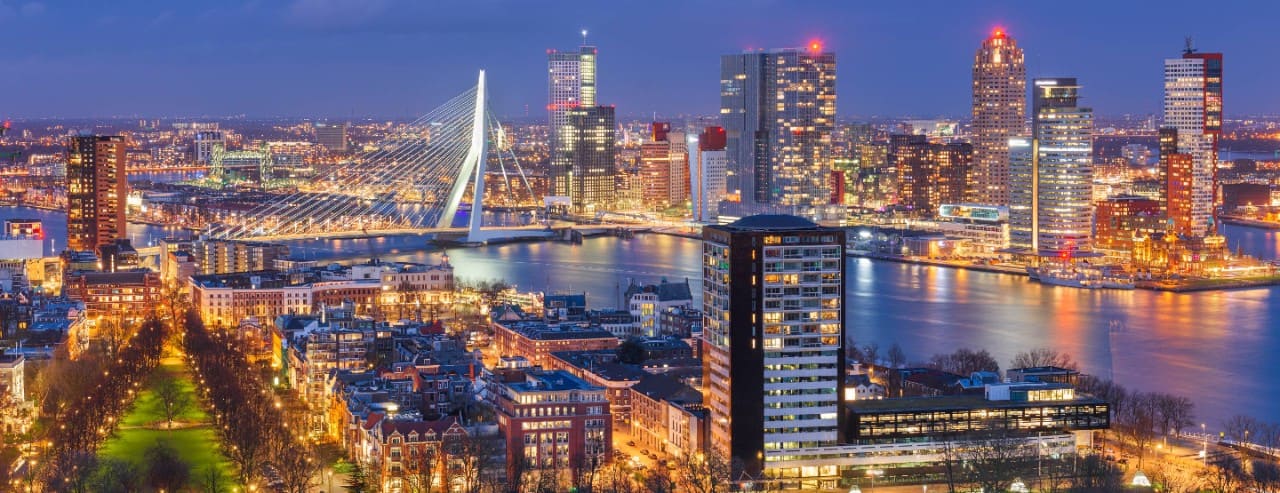 Rotterdam skyline at night with the Erasmus Bridge illuminated over the river.