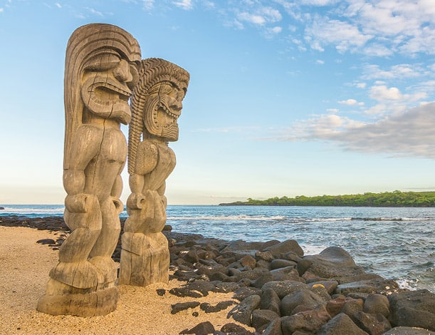 Two carved statues called Ki'i depicting the akua Kāne and Kanaloa stand outside of Hale o Keawe at the Puʻuhonua o Hōnaunau National Historical Park