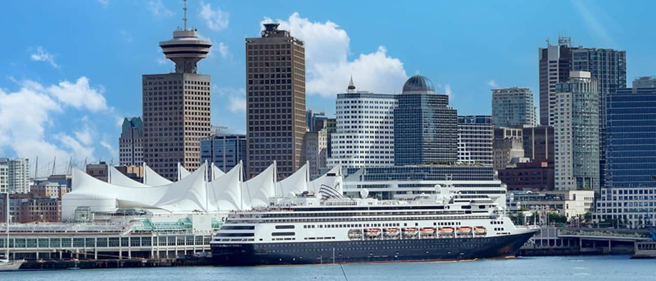 A Holland America cruise ship docked at Canada Place cruise ship port with Downtown Vancouver skyline in the background