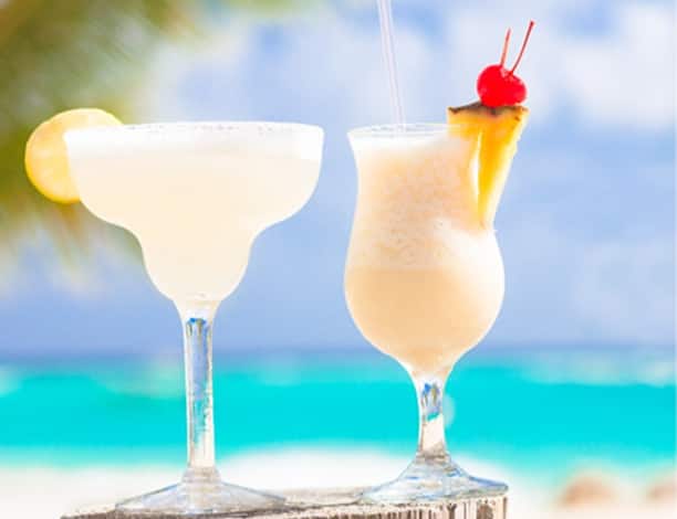Two cocktails placed on a wood board a sunny Hawaiian beach