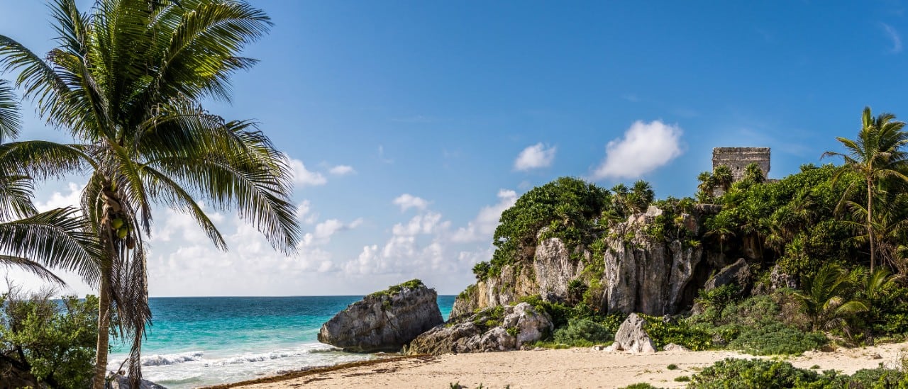 A scenic view of a Mazatlan beach with ancient ruins atop a small cliff