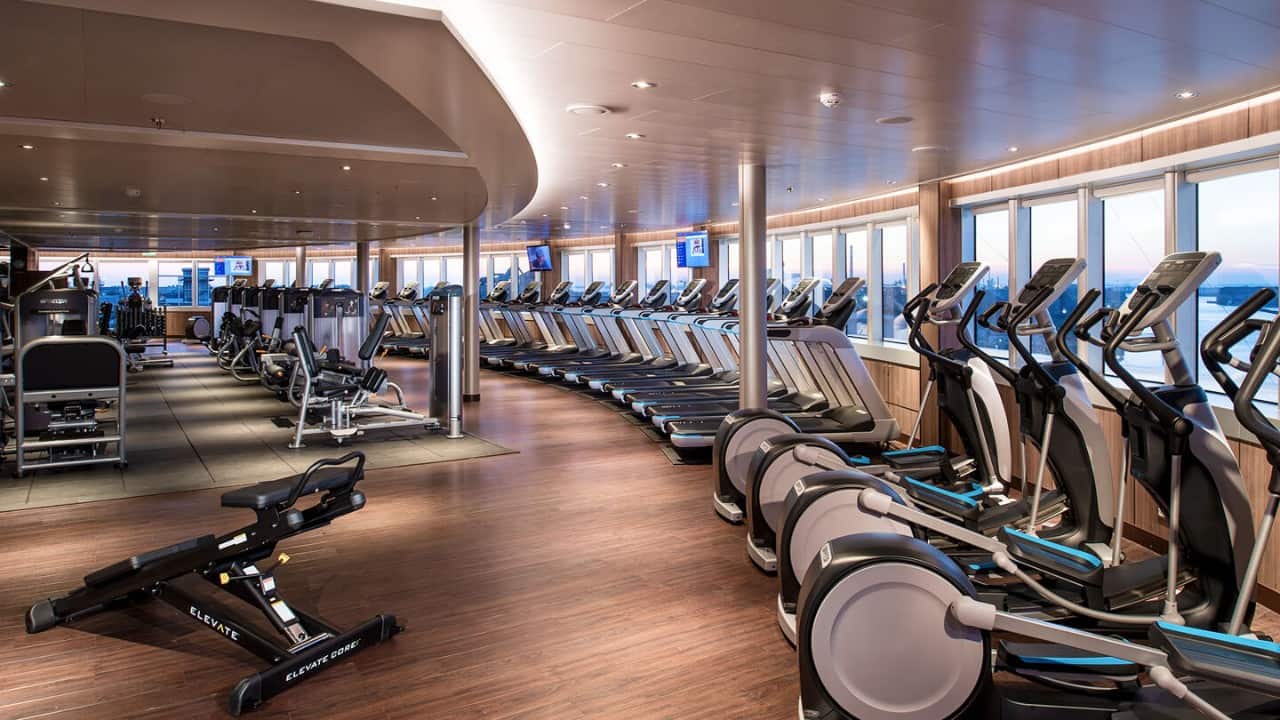 Spacious gym with rows of treadmills, elliptical machines, and strength equipment overlooking large windows.