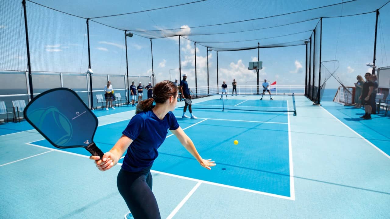 Guest playing pickleball on a cruise ship court with ocean in the background.