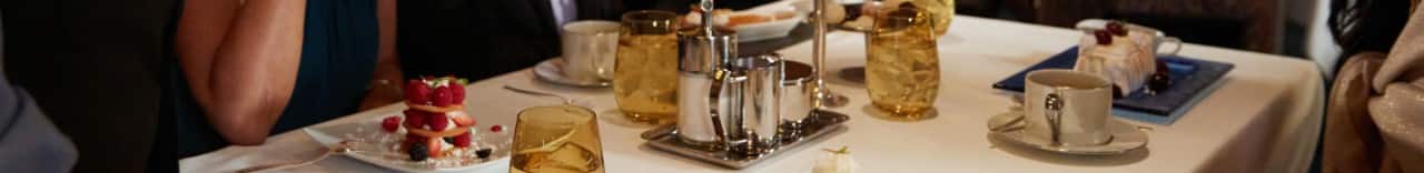 A man's elbow on a table full of food & drinks.