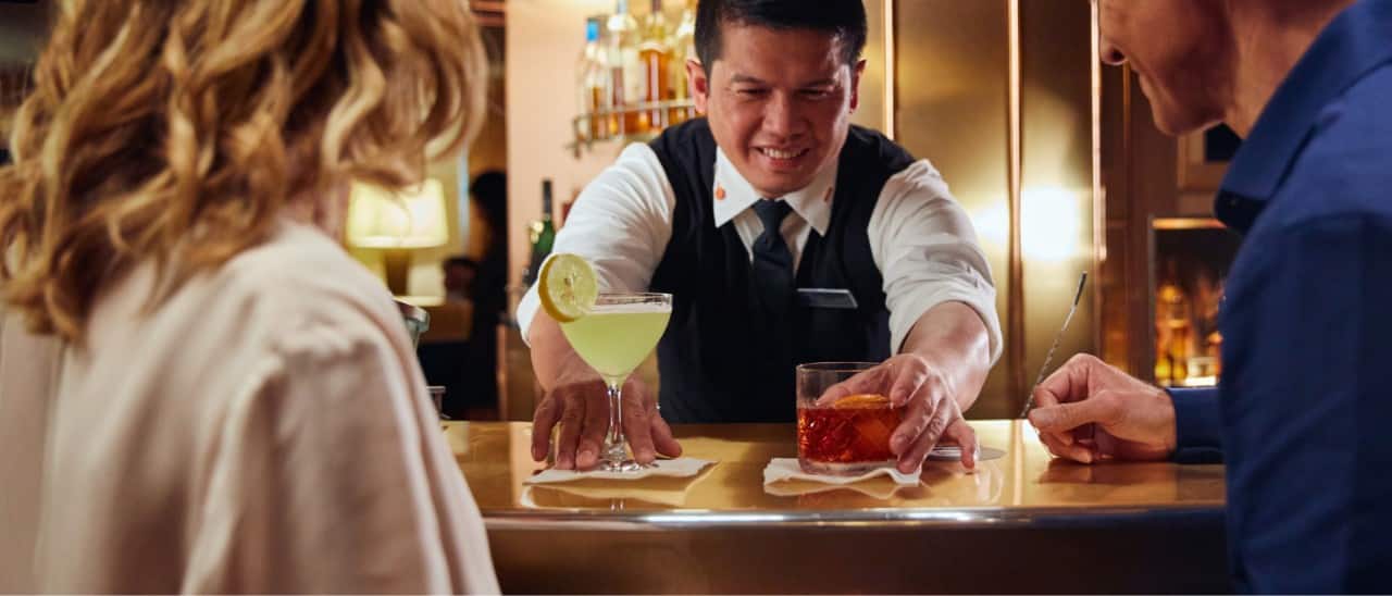 A bartender serving two drinks to a couple at the bar.