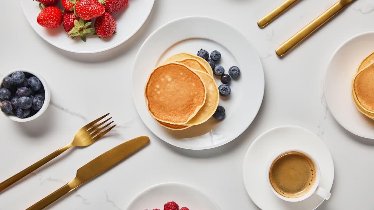 Fluffy golden pancakes served with fresh blueberries, strawberries, and coffee on a modern breakfast table, gourmet breakfast brunch dining experience.