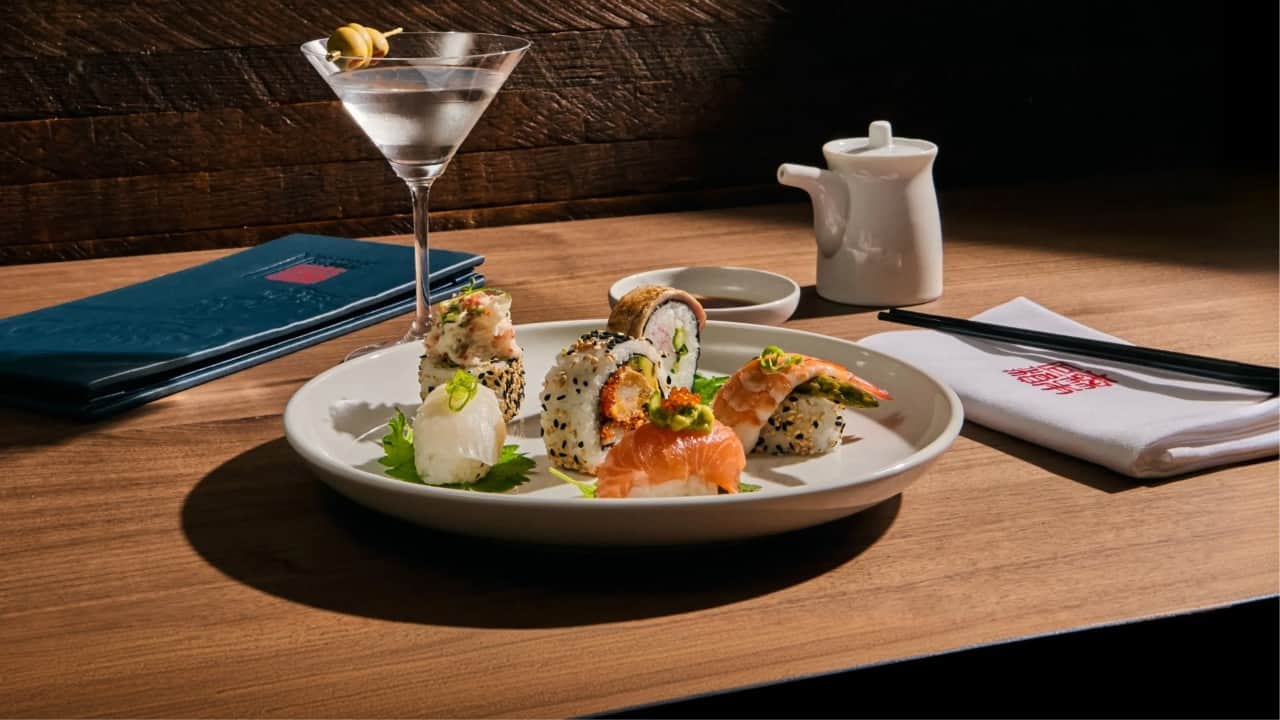 Assorted sushi and nigiri platter served with a martini, soy sauce, chopsticks, and a sake-style pitcher on a wooden restaurant table.