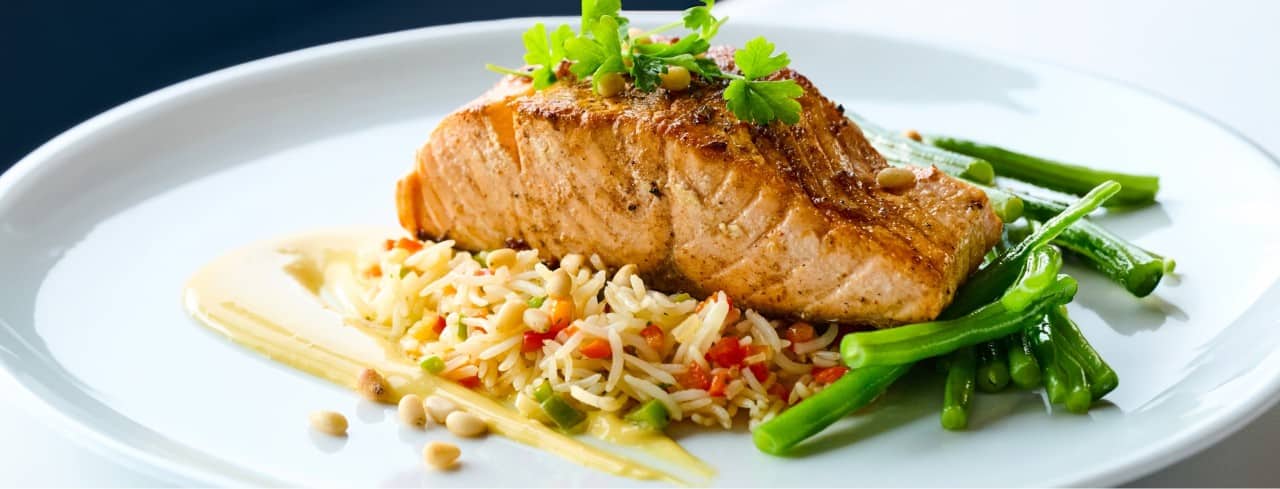 Seared salmon served with rice pilaf, green beans, and a light sauce.