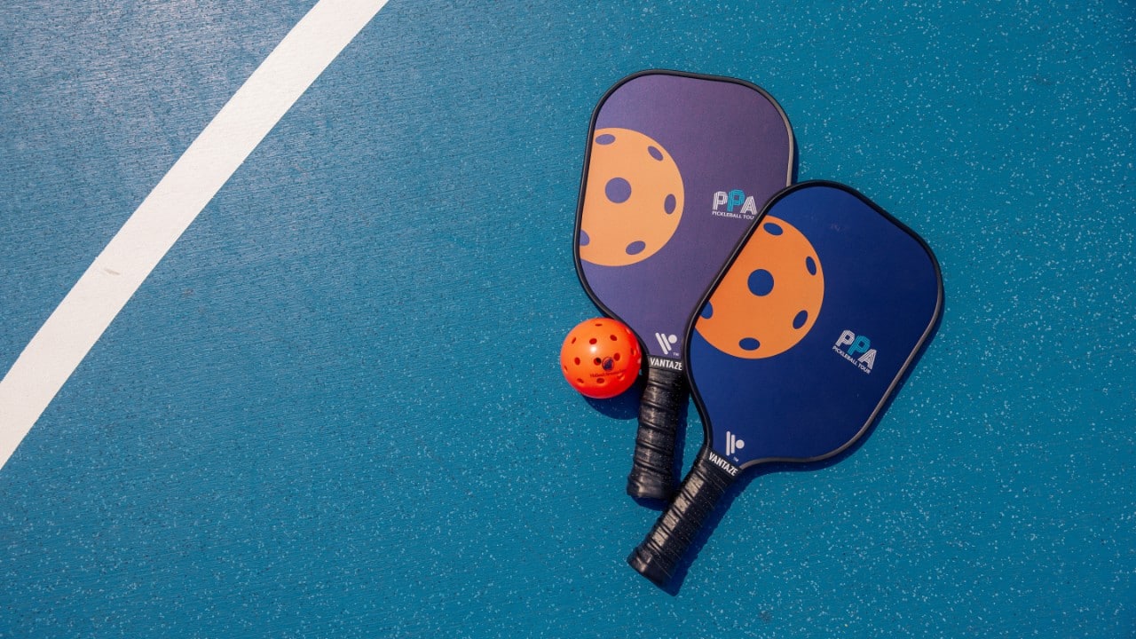 A ball and two pickleball rackets on a pickleball court.