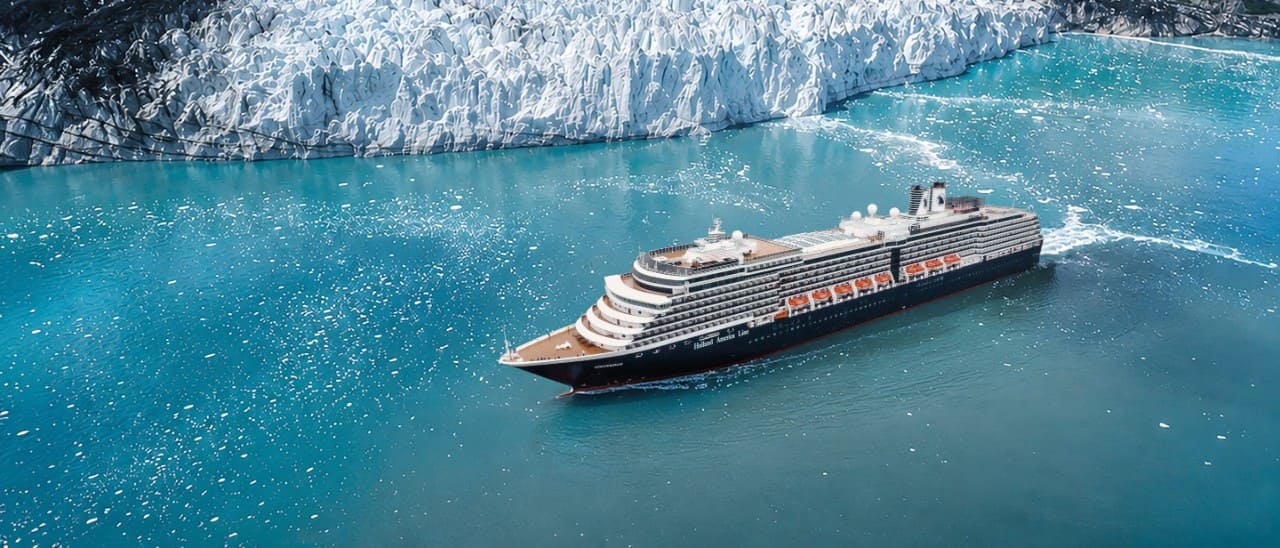 Cruise ship sailing through turquoise glacial waters alongside a towering Alaska glacier.
