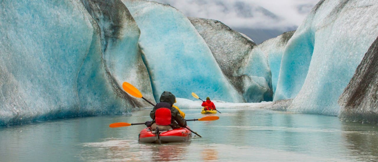 Kayakers paddling near blue ice in Alaska