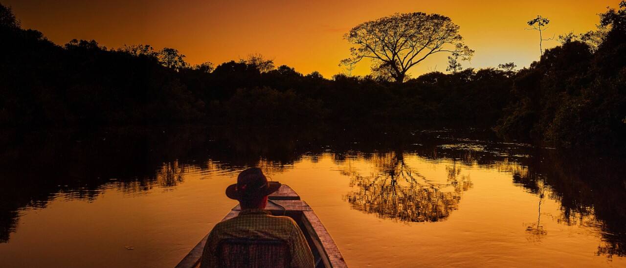 A main in a boat watching the sunset in the Amazon rainforest.